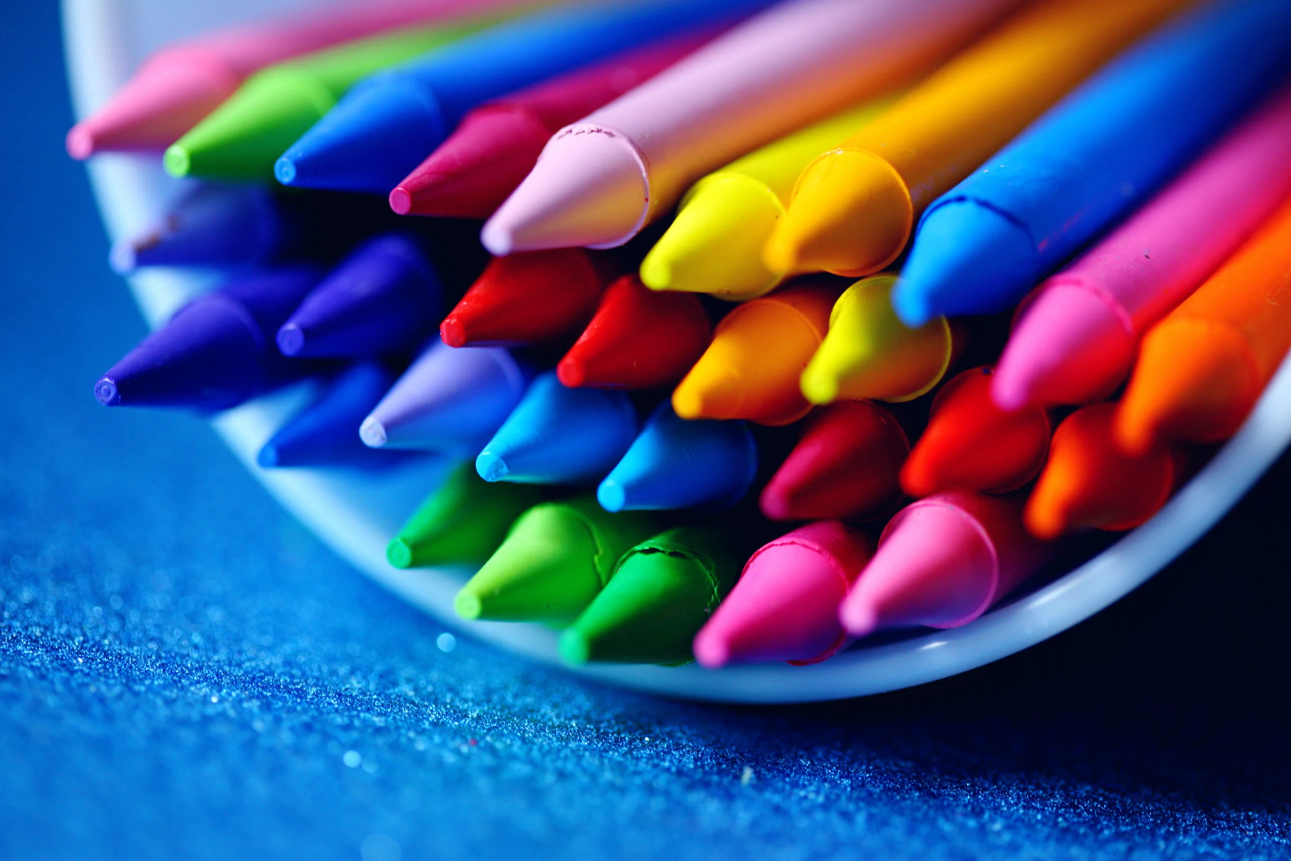 A close-up of vibrant colored crayons arranged in a bowl on a blue surface. jigsaw puzzle